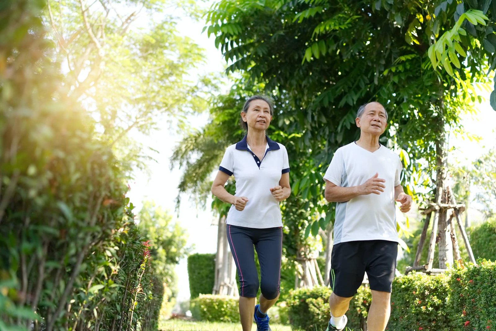 Asian Senior Couples Wearing White Sportswear Running In The Outdoor Park.