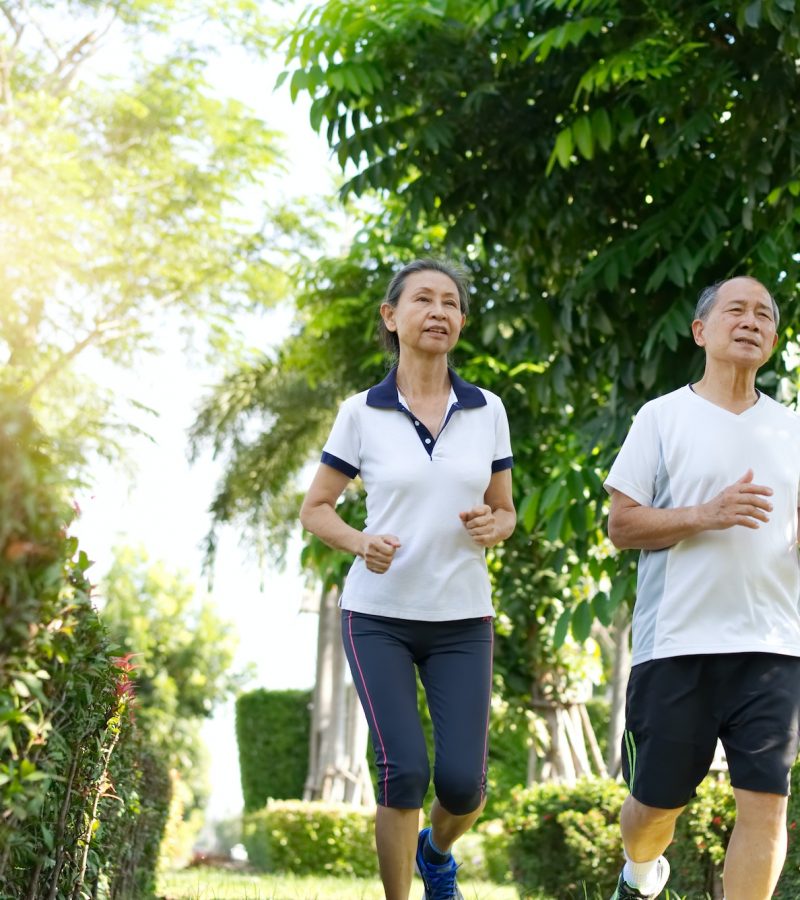 Asian senior couples wearing white sportswear running in the outdoor park.