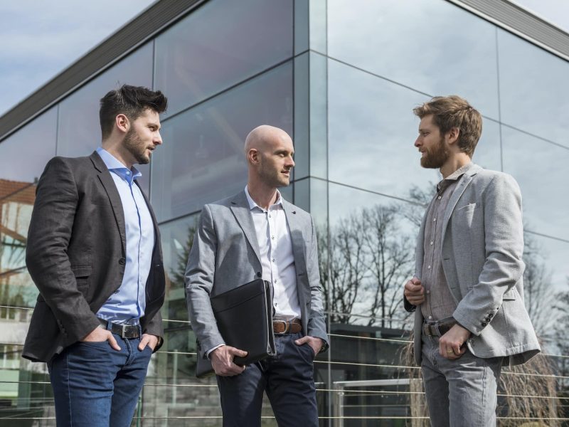 Three Businessmen Standing Outside Office Building Talking, Switzerland Golden Visa Consultancy